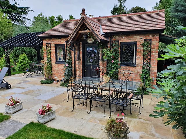 Brick garden room with a sandstone patio, wrought-iron dining set and fig tree in a Surrey garden