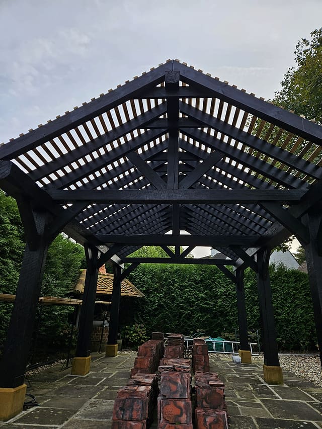 View up into the green oak roof trusses of a garden gazebo over a wet flagstone patio in Surrey