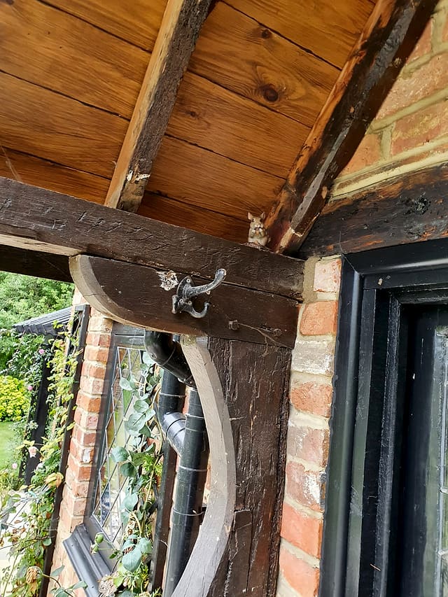 Close-up of a timber pergola corbel and beam with a cast-iron hook against brickwork on a Surrey garden room
